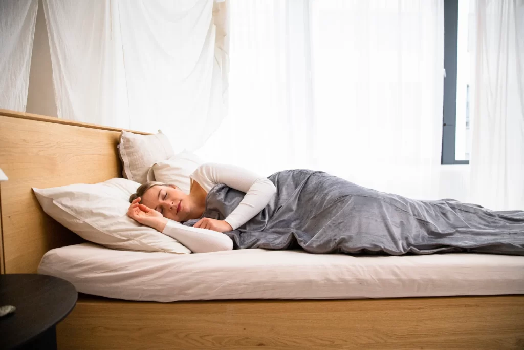 Vrouw slaapt in een lichte slaapkamer, passend bij het belang van minder schermlicht voor een betere nachtrust.
