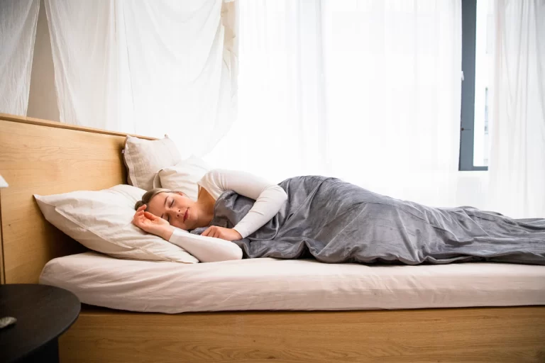 Vrouw slaapt in een lichte slaapkamer, passend bij het belang van minder schermlicht voor een betere nachtrust.